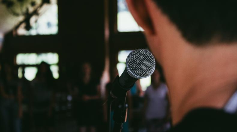 back of someone's head standing in front of microphone facing a crowd of people 