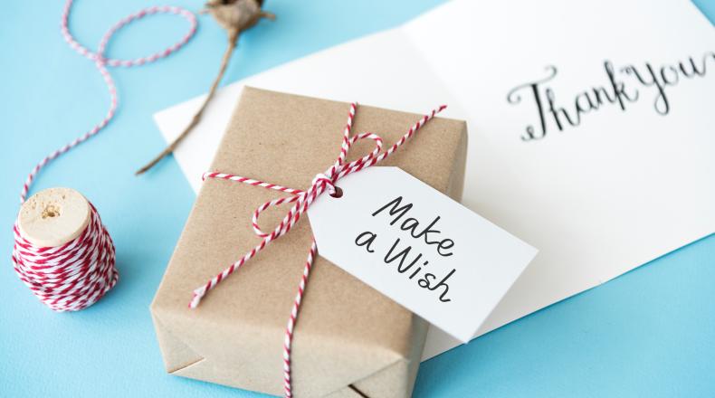 Small package wrapped in brown paper with tag that says make a wish on top of an envelope that says thank you