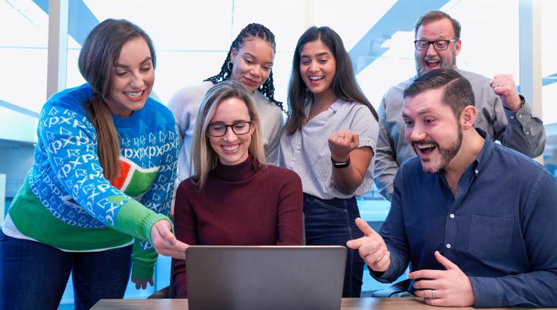 men and women sitting and standing staring at a laptop