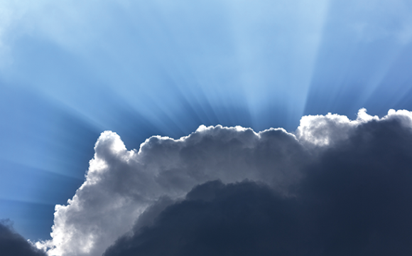 Rays of sunlight coming from behind a cloud in a blue sky.