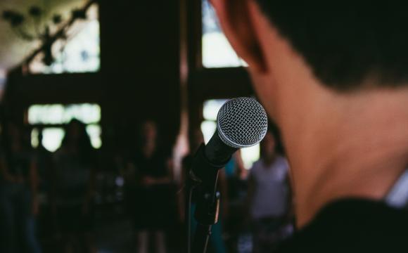 back of someone's head standing in front of microphone facing a crowd of people 