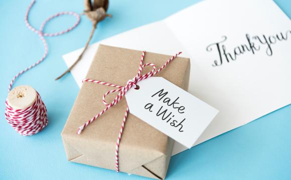 Small package wrapped in brown paper with tag that says make a wish on top of an envelope that says thank you