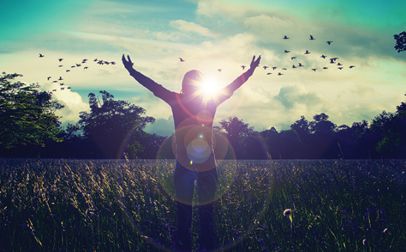 person standing in a field with their arms up to the sky