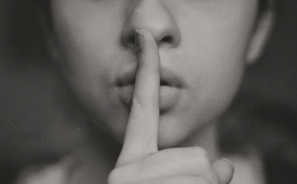 woman with her finger to her lips symbolizing to be quiet