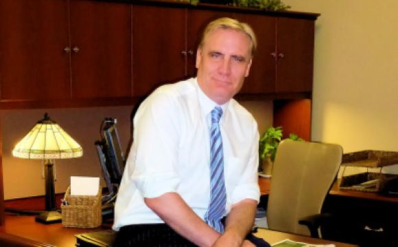 man in a white shirt and blue tie leaning against a desk