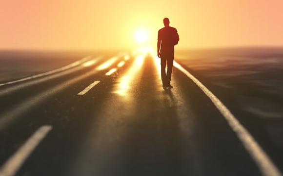 silhouette of a man walking down a road at sunset