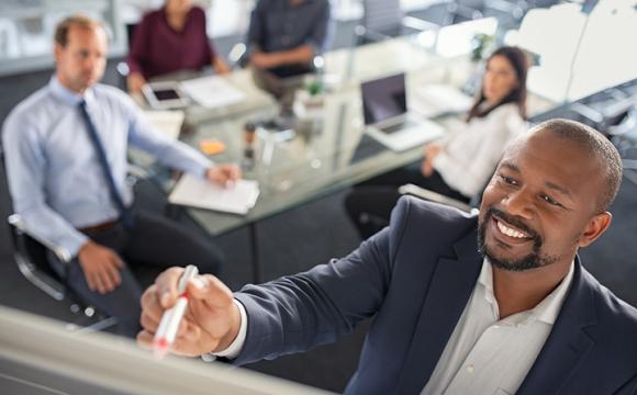 businessman writing on a board in front of other people