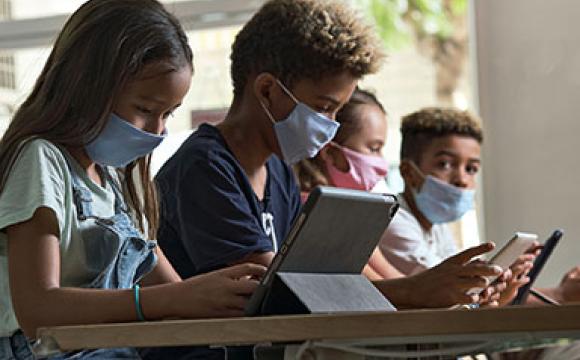 four diverse kids in masks working on ipads