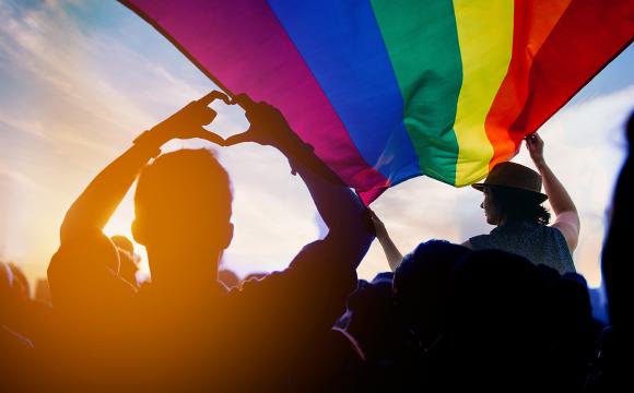 people marching holding a rainbow flag and making a heart symbol