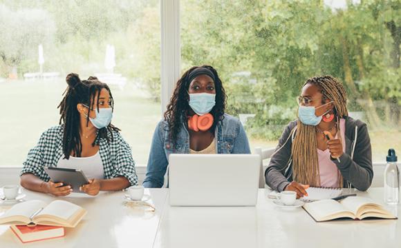 three black women at a table with a laptop and books