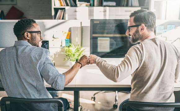 white man and a black man wrist bump in an office