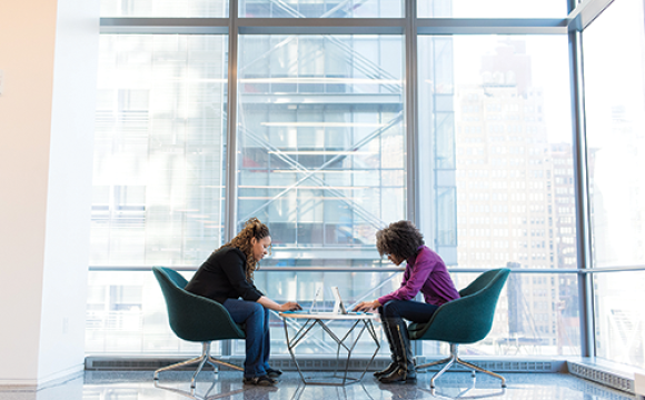 two women sitting at a table having a discussion by a large windor