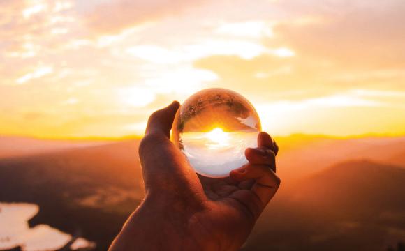 hand holding a crystal ball with a sunset and mountains in the background