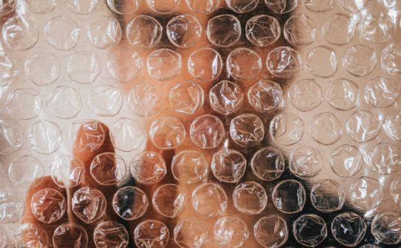 man behind bubble wrap with his fingers pressed to it