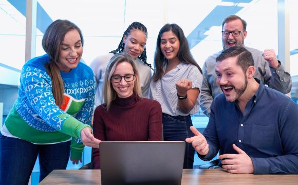 men and women sitting and standing staring at a laptop