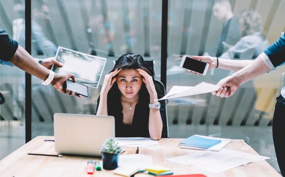 woman holding her head with people handing her papers