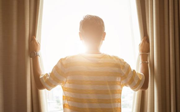 person pulling back curtains looking out a window